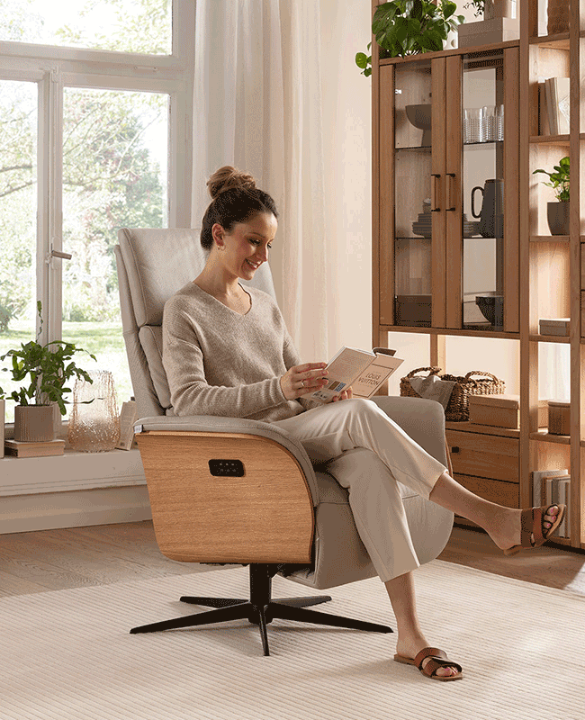 Frau entspannt in beigem Relaxsessel mit Holzakzenten, legt die Beine hoch und liest ein Buch.