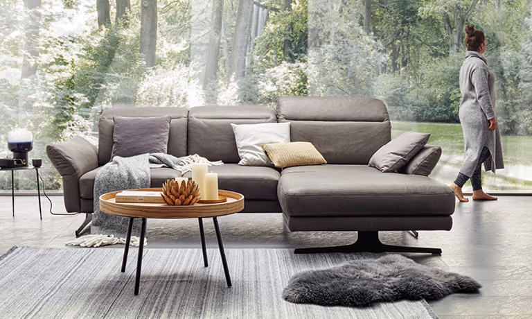 Sitzbank aus Holz, Ledersofa im Wohnzimmer auf hellem Teppich mit Couchtisch aus Holz und Vasen in verschiedenen Größen mit Blumen