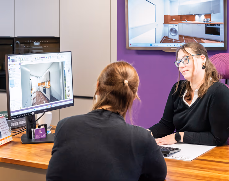 Mitarbeiterin von Kuechenhaus Gruber zeigt Kundin 3D-Plan einer Kueche am Computer