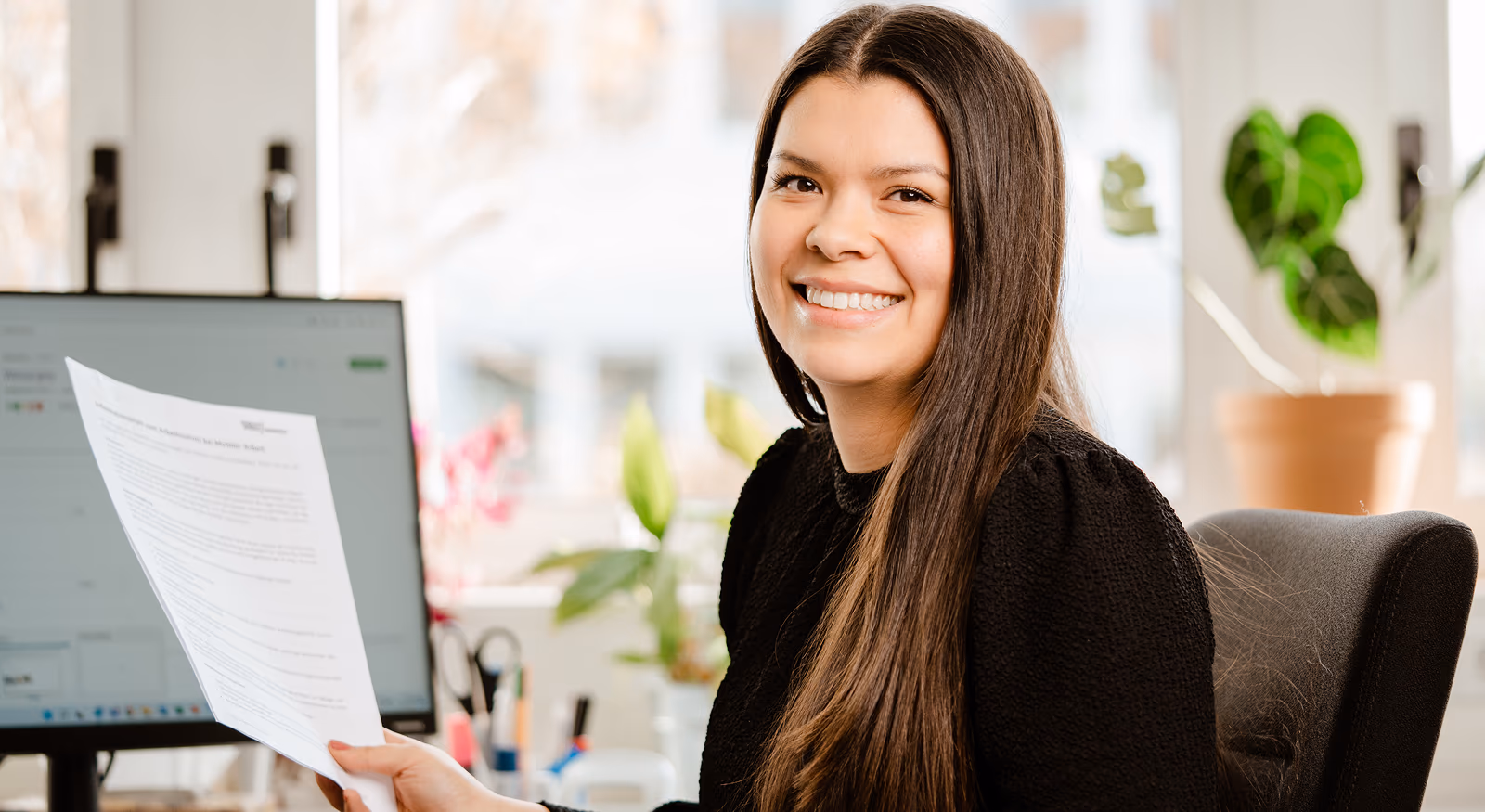 freundliche Frau am Laptop mit Papier in Hand
