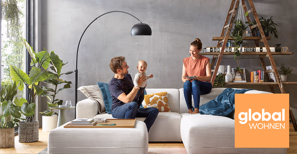 Frau und Mann mit Kleinkind auf einem modernen grauen Sofa im Wohnzimmer - gut gelaunt