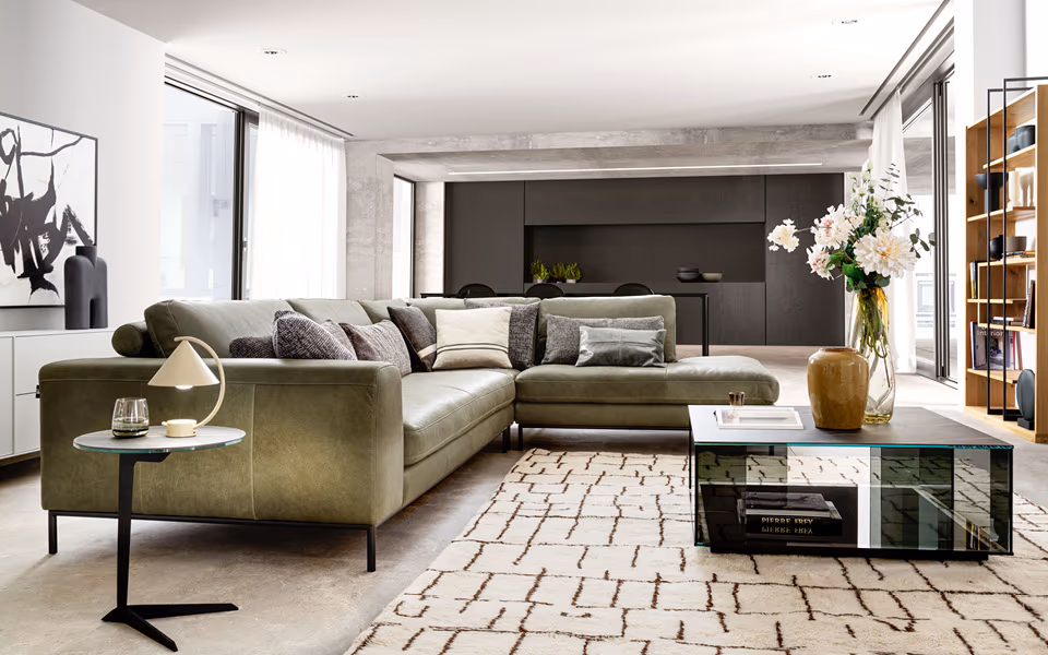 Wohnzimmer Ansicht mit Ledercouch in olivegrün und gläsernen Couchtisch.