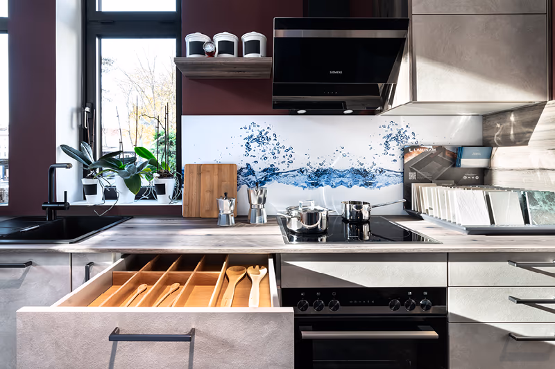 Helle Contur Kuechenzeile mit geoeffneter Schublade und Dunstabzugshaube.