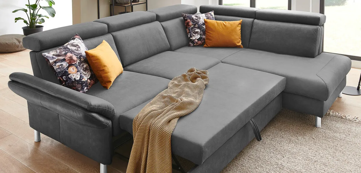 Komfortables Funktionssofa in dunklem Grau mit Schlaffunktion zum Sitzen und Liegen, Mann sitzt auf Ledersofa im Wohnzimmer 