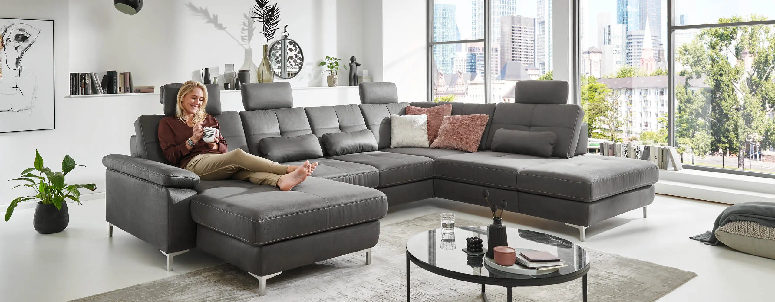 Frau mit Tasse liegt auf grauem Sofa