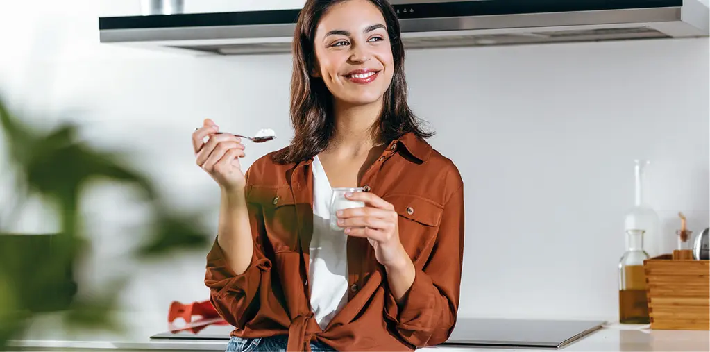 Frau probiert Joghurt in moderner Küche, Headerbild kleine Küchen.