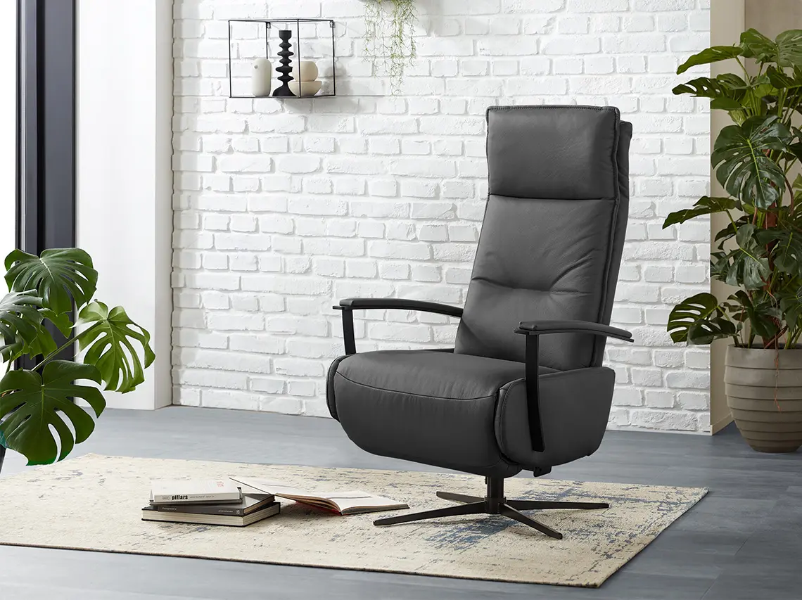 Dunkelgrauer Ledersessel mit Relaxfunktion vor einer weißen Ziegelwand.