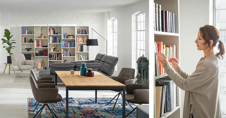 Großraumwohnung mit Bücherregal im Hintergrund und Esstisch im Vordergrund. Eine Frau stöbert im Bücherregal.