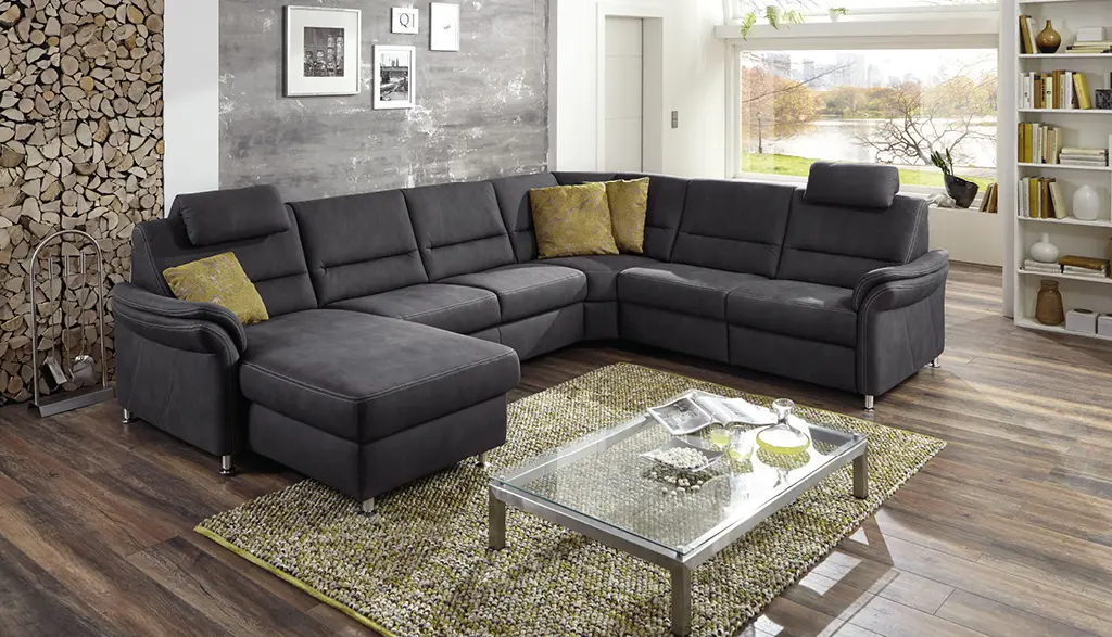 Großzügiges U-förmiges Sofa in Dunkelgrau von Couchliebe mit verstellbaren Kopfstützen und gelben Zierkissen in modernem Wohnzimmer mit Holzboden – erhältlich bei Möbel Rommel.