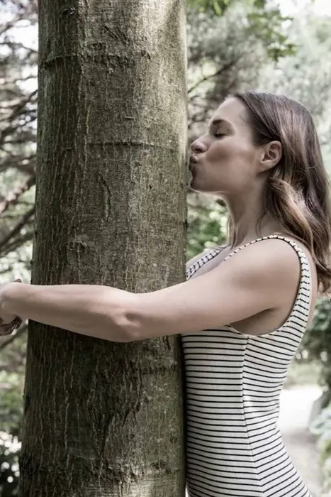 Frau ist im Wald und umarmt und küsst einen Baum. 