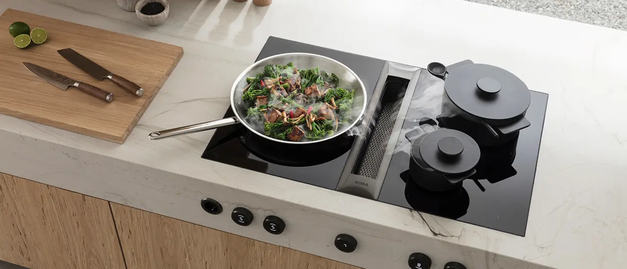 Bratpfanne mit Töpfen auf Herdplatte mit Muldenlüfter