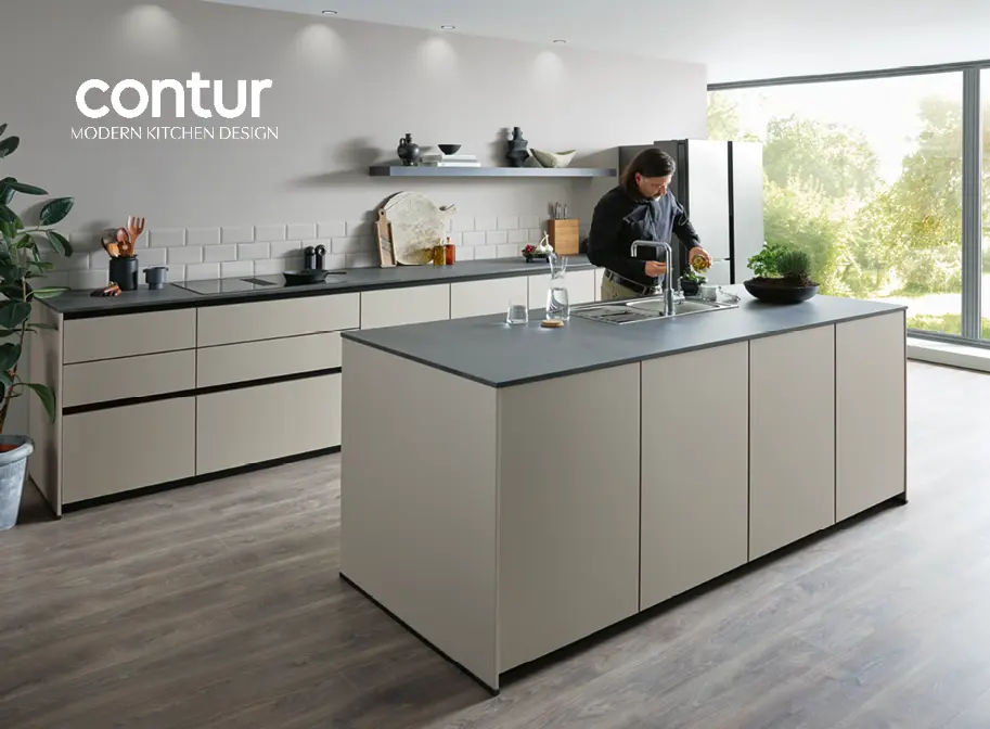 Hellgraue grifflose Küche mit Kücheninsel von contur Küchen. Ein Mann steht vor der Kücheninsel und bereitet etwas vor der Waschgarnitur vor.