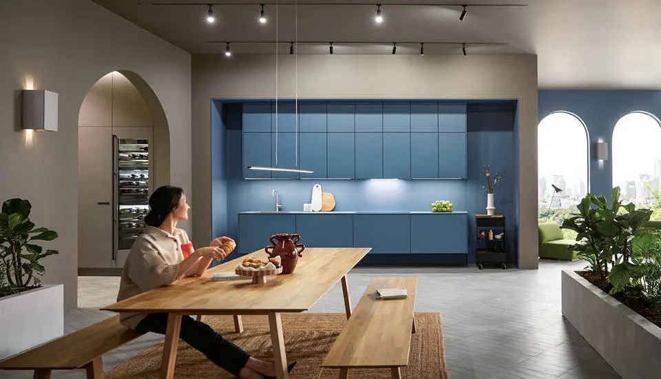 Frau am Esstisch mit moderner Küche im Hintergrund