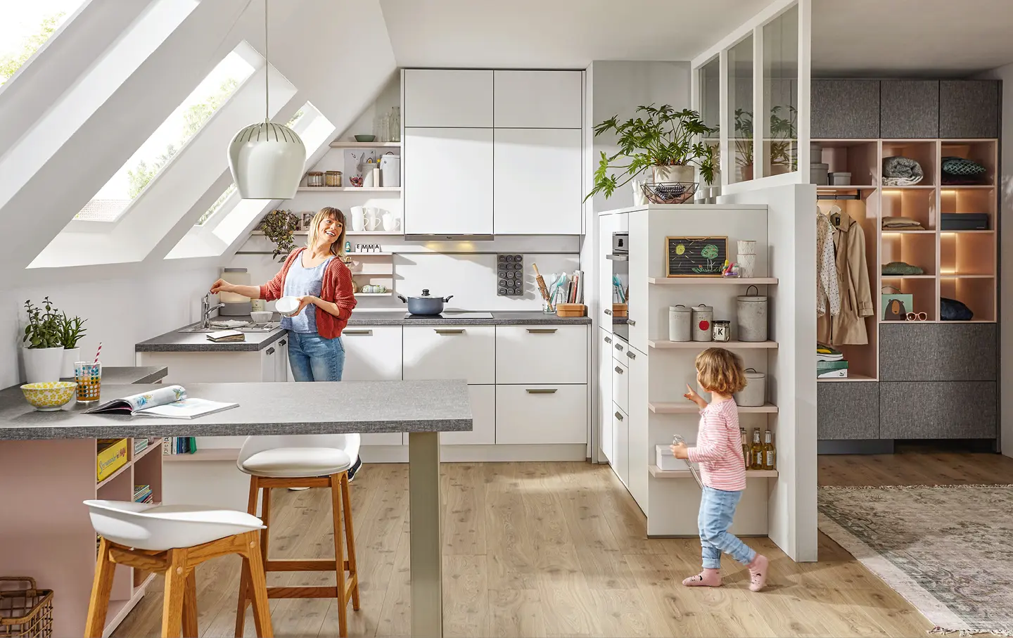 Mutter mit Tochter in heller Winkelkueche mit Dachschraege und Tischelement mit Barhockern