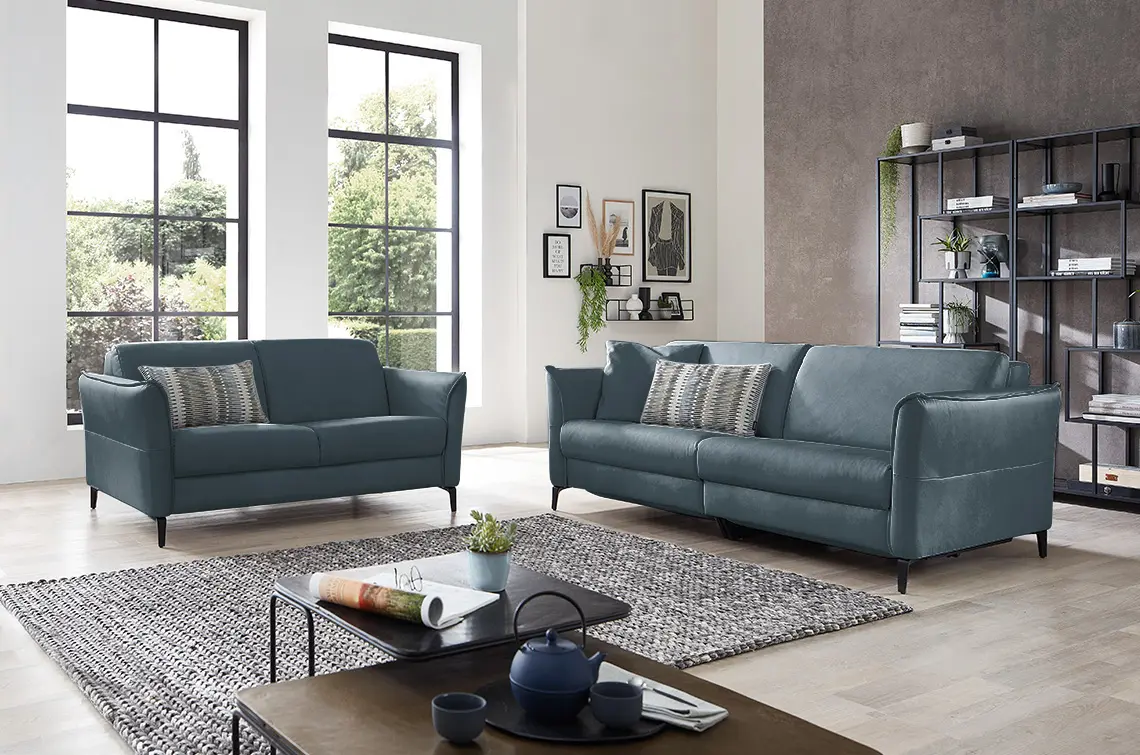 Zwei petrol farbene Sofa Garnituren in einem hellen gemütlichen Raum.