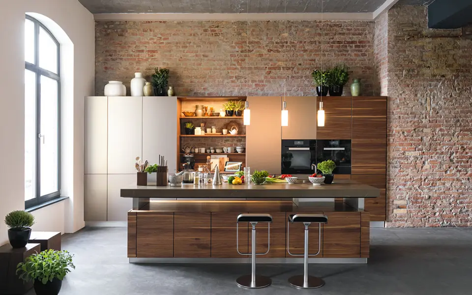 Vorderansicht einer Küche aus Holz mit einem unverputztem Mauerwerk im Hintergrund.
    