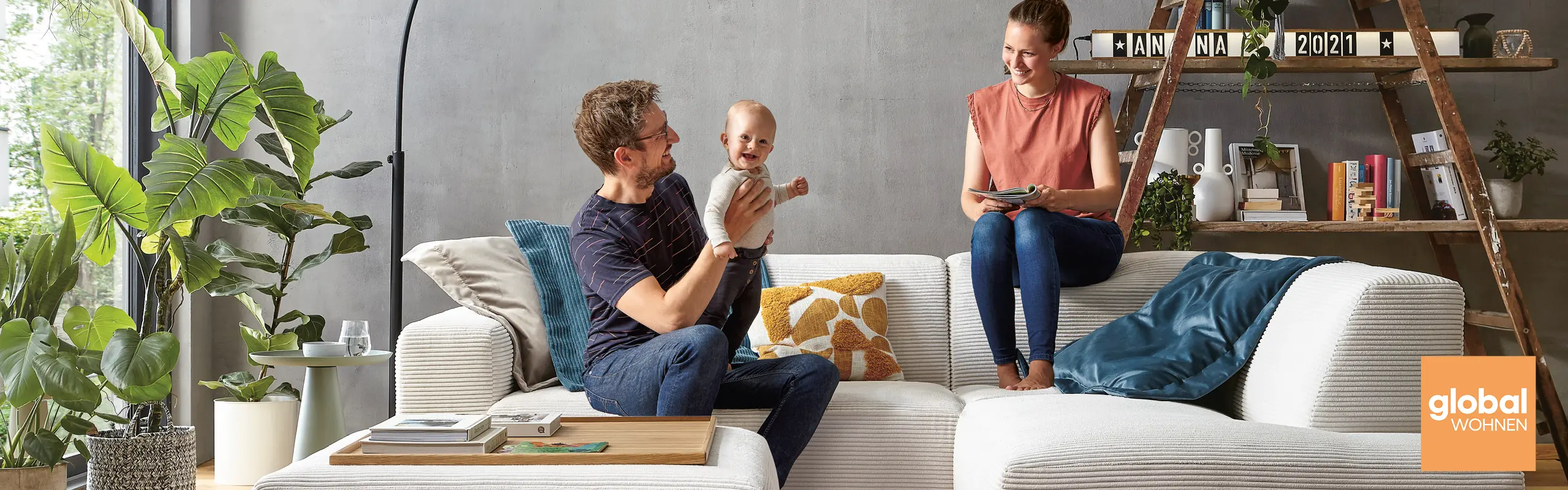 Frau und Mann mit Kleinkind auf einem modernen grauen Sofa im Wohnzimmer - gut gelaunt