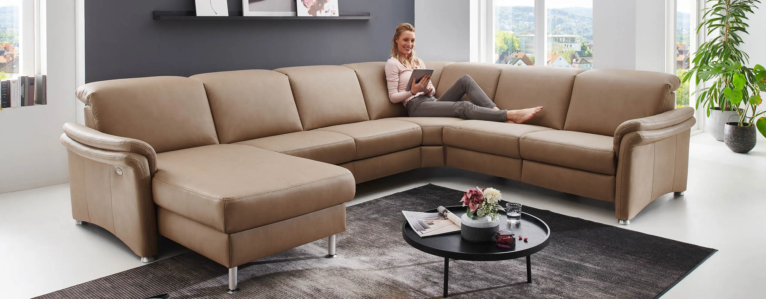 Frau liest auf beigem Leder-Ecksofa