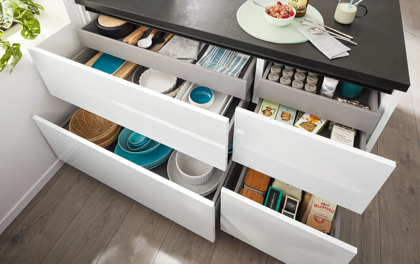 Kuecheninsel mit dunkelgrauer Arbeitsplatte und geoeffneten Schubladen gefuellt mit Geschirr und Kuechenutensilien
