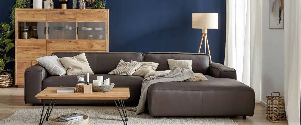 Dunkelbraunes Ledersofa vor blauer Wand mit Holzsideboard und Couchtisch