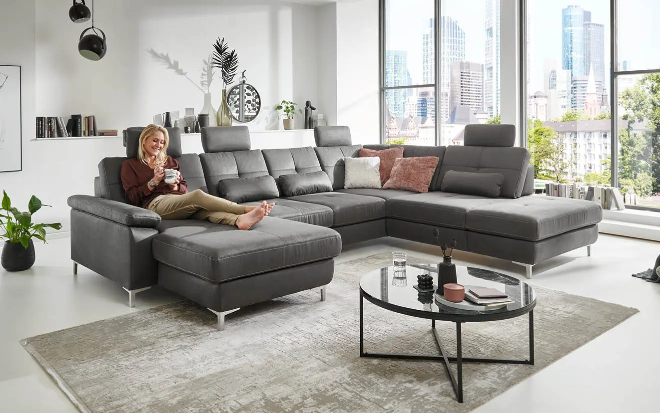 Frau mit Tasse liegt auf grauem Sofa