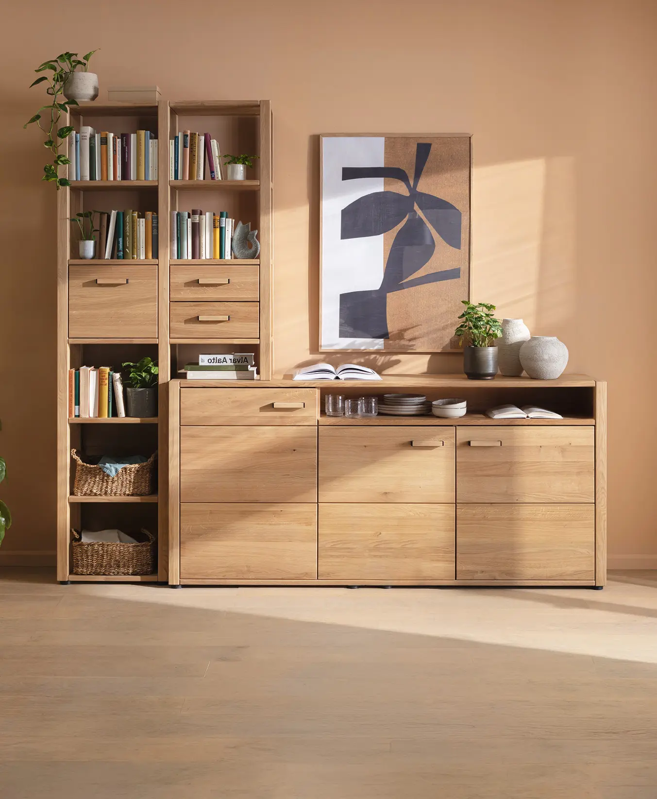 Helle Holz-Regalwand mit Büchern und Sideboard unter einem Wandbild
