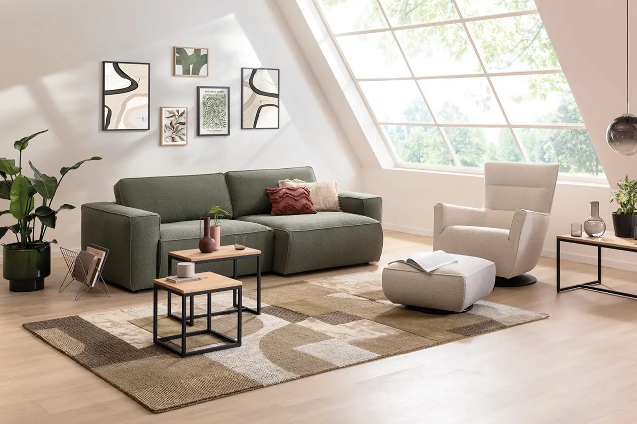 Heller Wohnbereich mit modernem Sofa, bequemen Relaxsessel, Couchtischen und Teppich, große Fenster sorgen für Tageslicht, wohnliche Einrichtung mit natürlichen Farben und klaren Formen