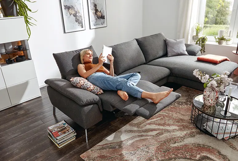 Frau entspannt auf dunkelgrauem Sofa Global Gotera, das auf Teppich und dunklem Fußboden steht