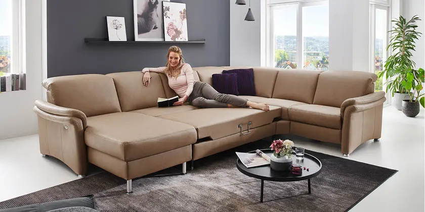 Frau liegtauf beigem Leder-Ecksofa mit Liegefläche