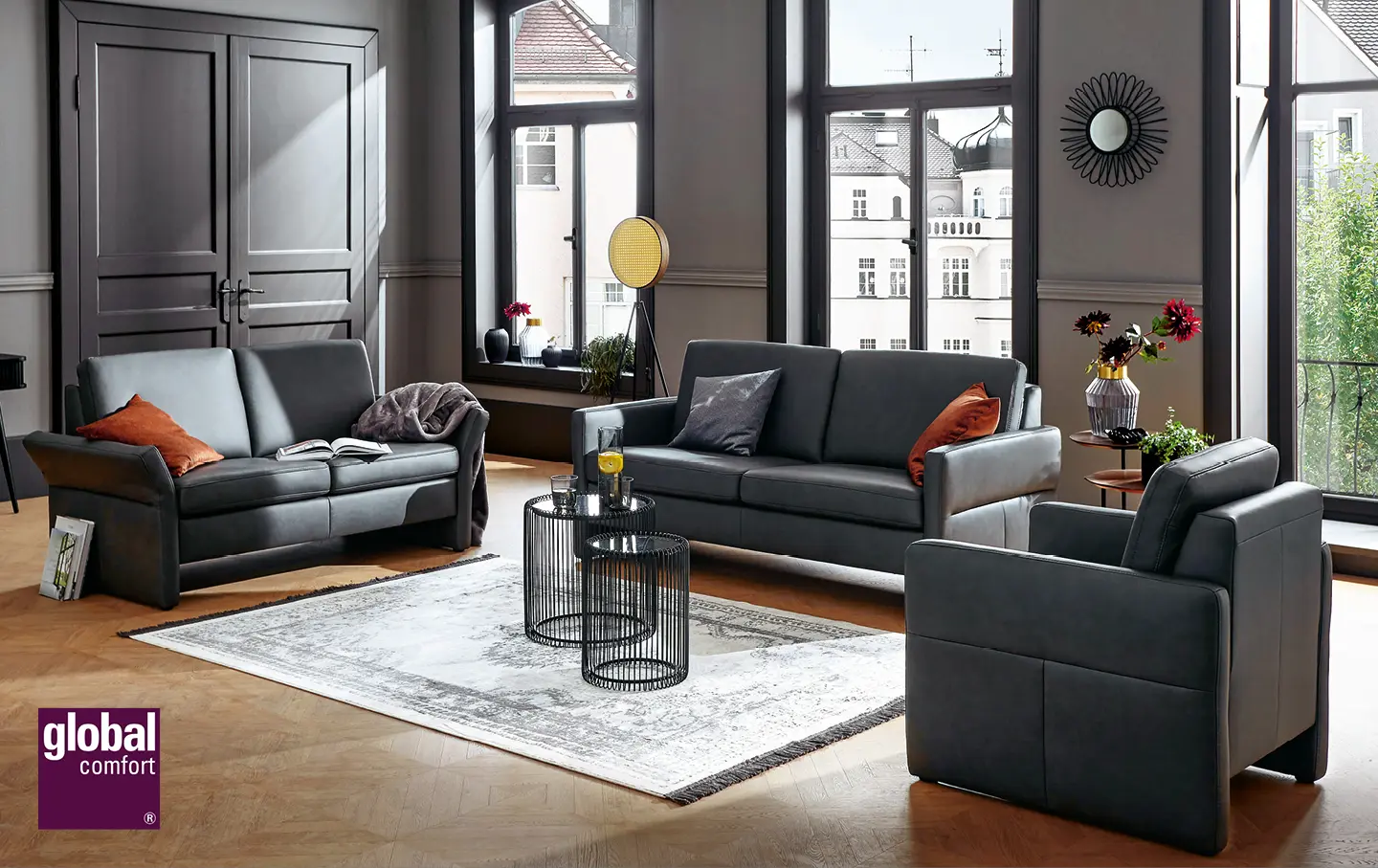 2 dunkelgraue Ledersofas mit passendem Ledersessel und orangefarbenen Kissen in geraeumingem Wohnzimmer.