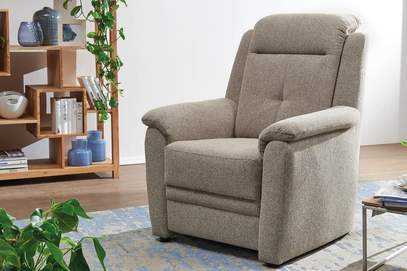 Cremefarbener Polstersessel vor hoelzernem Regal in gemuetlichem Wohnzimmer