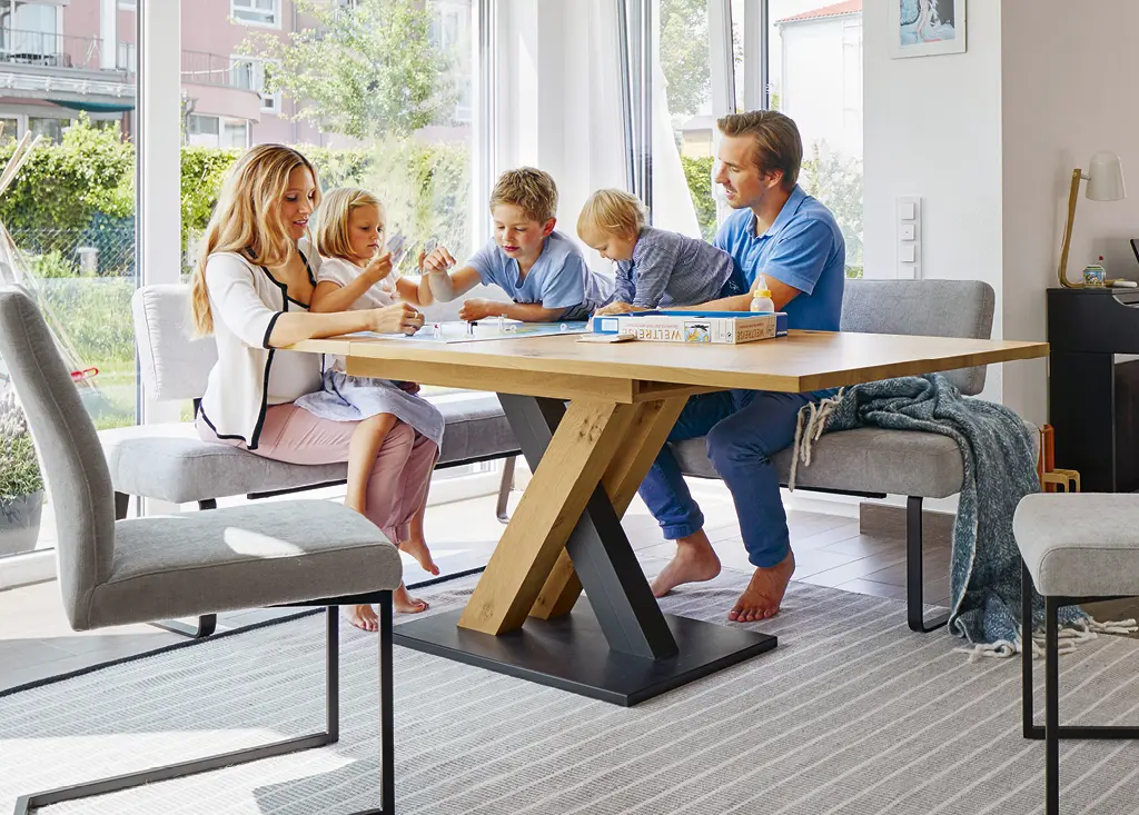 Familie sitzend an hölzernem Esstisch mit grauen Stühlen spielen Gesellschaftsspiel im Esszimmer