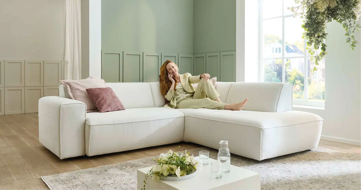 Frau entspannt auf heller Lounge-Eckcouch im Wohnzimmer, Couchliebe Lounge.