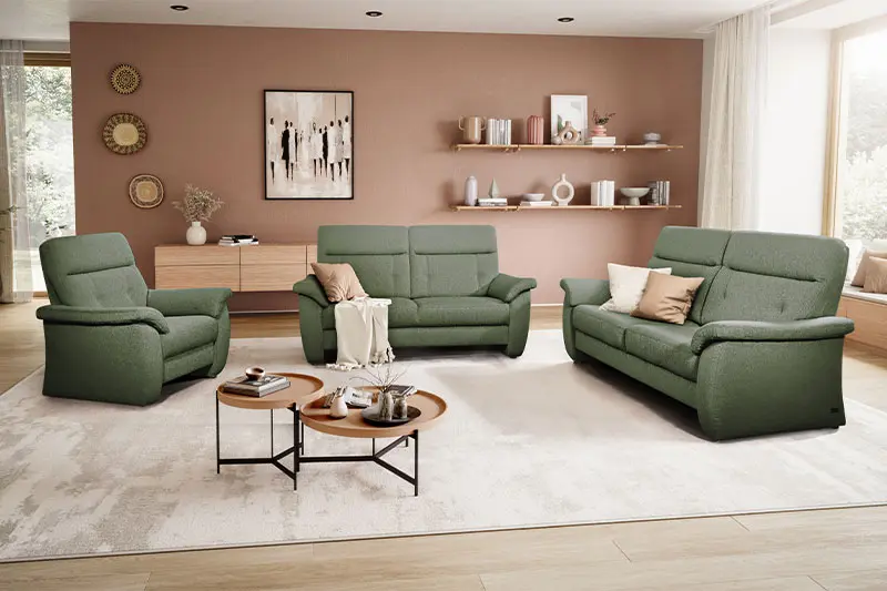 Grüner Sessel, neben zwei grünen Couch Garnituren in einem hellen gemütlichen Raum.