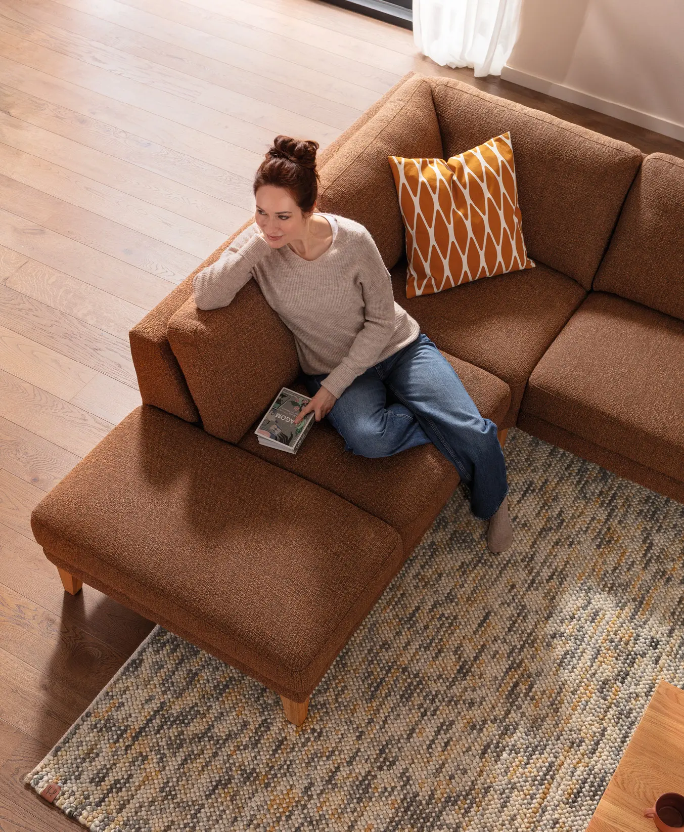 Frau sitzt mit Buch auf braunem Ecksofa im Wohnzimmer