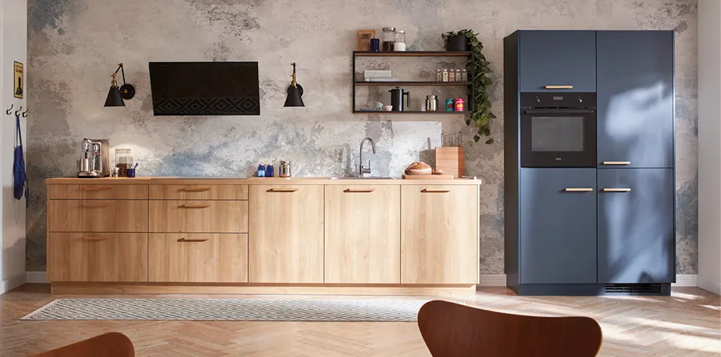 Moderne Küche mit hellen Holzfronten, blauen Hochschränken und integrierten Elektrogeräten. Klare Linien, offene Regale und strukturierte Wandfläche schaffen ein hochwertiges Küchendesign für zeitgemäßes Wohnen.