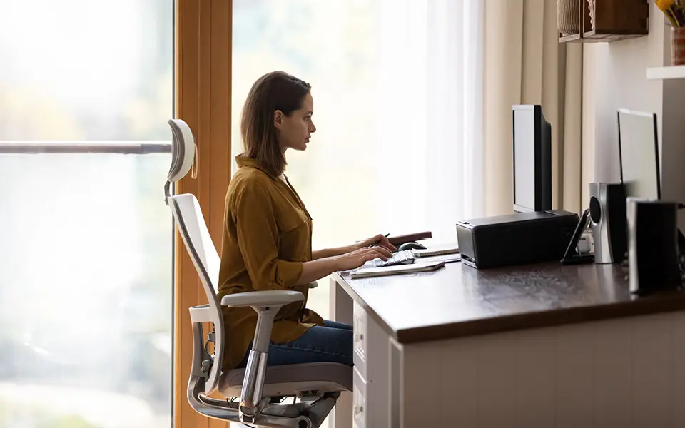 Frau sitzt in ergonomischer Haltung am Schreibtisch.