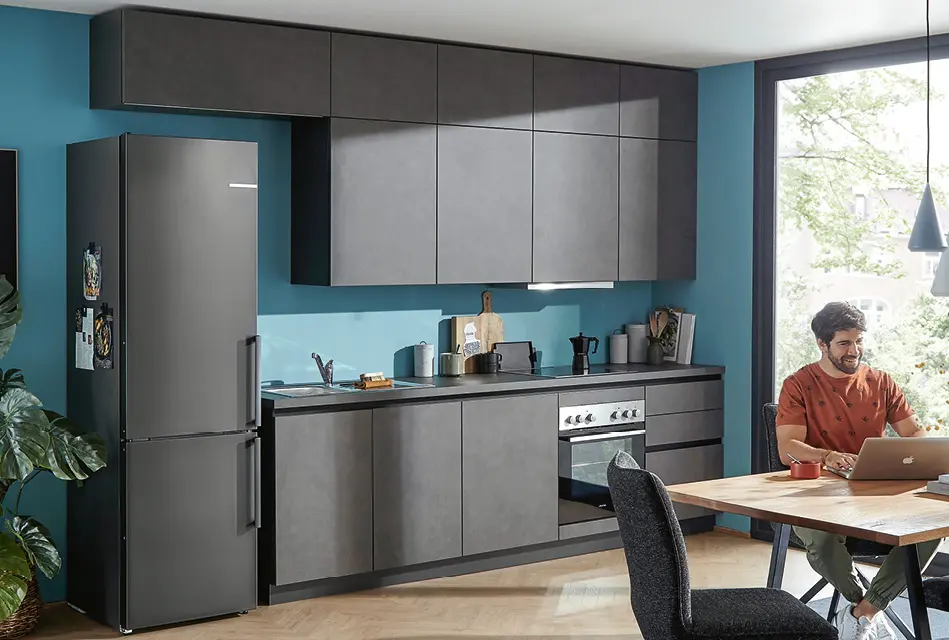 Kompakte Küchenzeile mit grauen Fronten und Kühlschrank im Wohnraum.