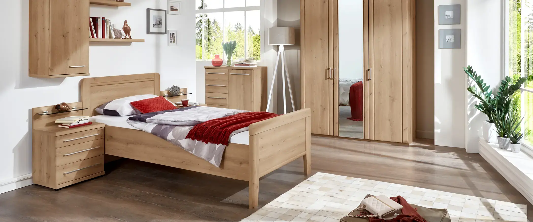 Holzbett mit roter Decke, Nachttischen, Kommode, Kleiderschrank und großer Fensterfront