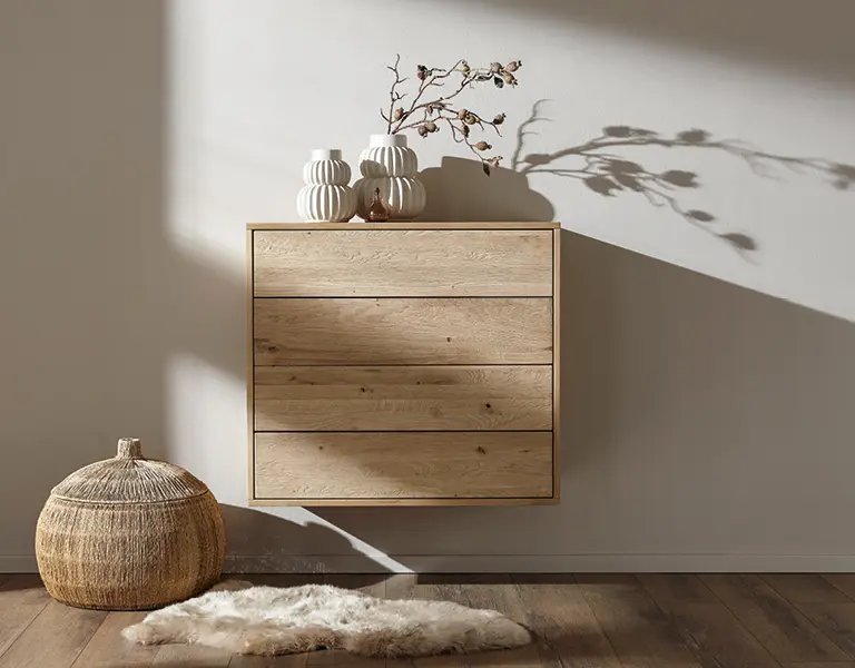 Schwebende Kommode aus Holz an der Wand mit dekorativen Vasen, davor ein Lammfell