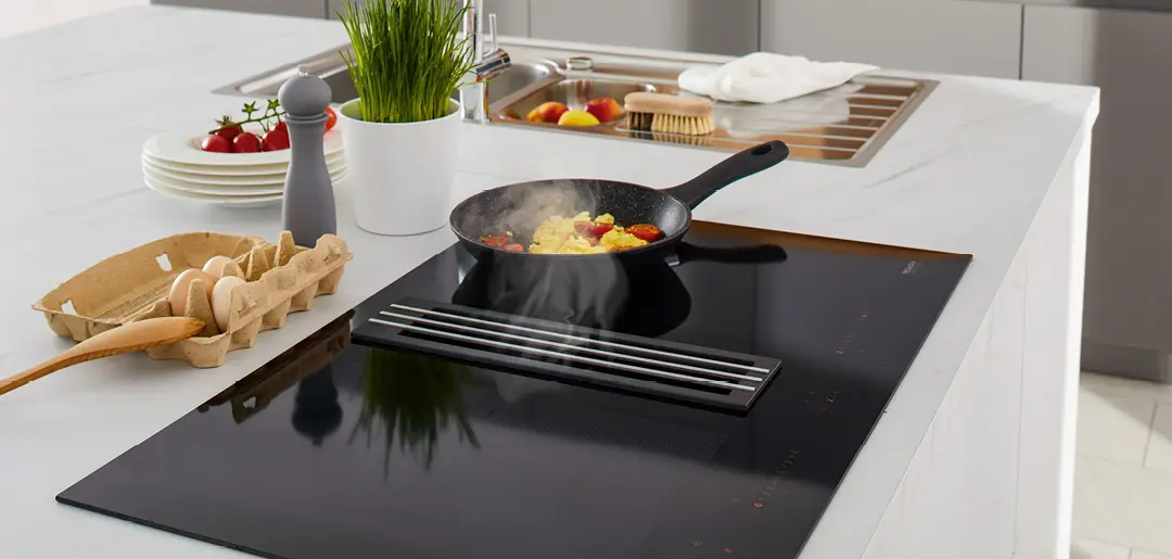 Induktionskochfeld mit Muldenlüfter umgeben von einer weißen Arbeitsfläche in einer Küche von Global Küchen