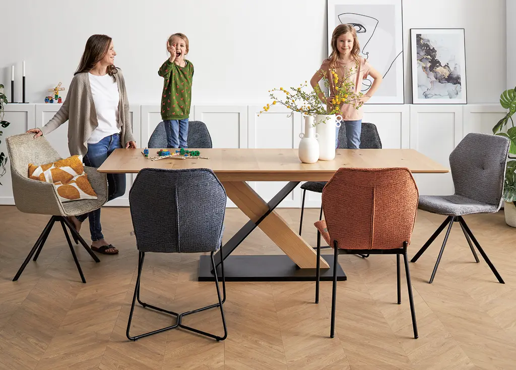 Mutter mit Töchtern an hölzernem Esstisch und Stühle mit buntem Bezug im Esszimmer