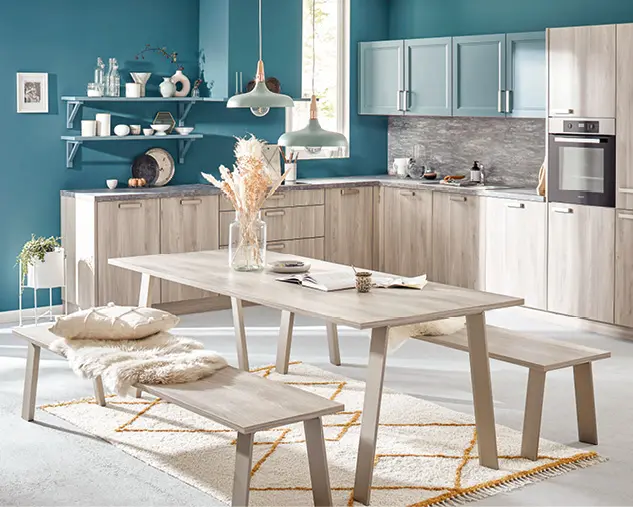Helle Wohnküche mit Einbauküche in Holzoptik, offenen Regalen und Essgruppe mit Tisch und Bänken. Moderne Küche mit gemütlicher Sitzgelegenheit, Dekoration und viel Tageslicht für gemeinsames Kochen und Essen.