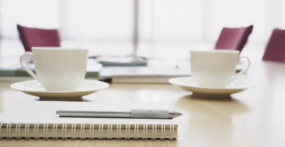 Beratungssituation mit Kaffeetassen, Notizblock und Stift