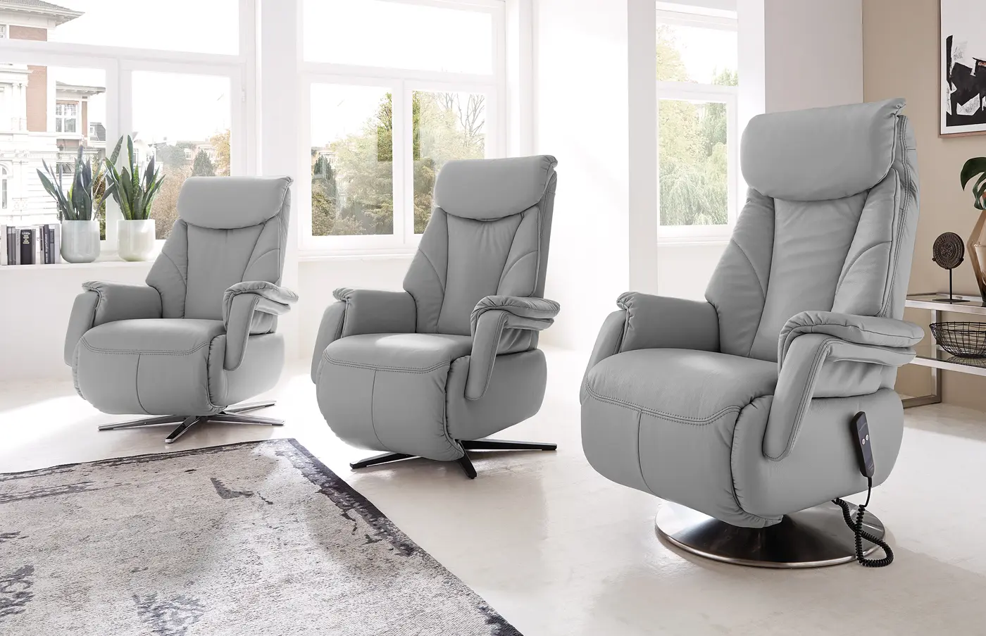 Drei graue Relaxsessel mit unterschiedlichen Fußgestellen in einem hellen Raum.