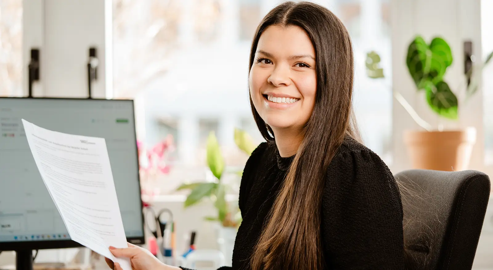 freundliche Frau am Laptop mit Papier in Hand