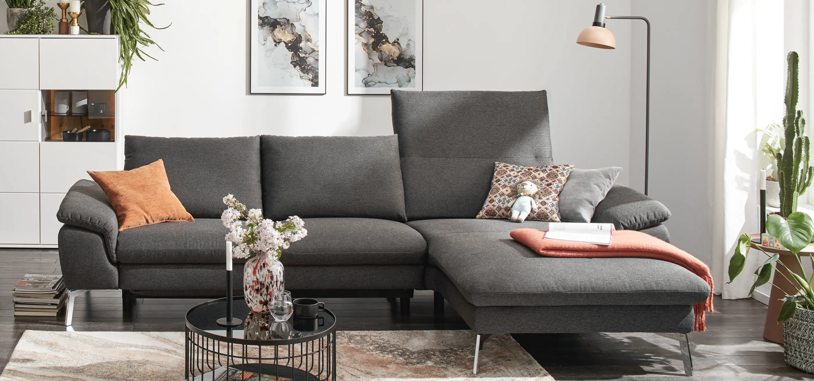 Anthrazitfarbenes Sofa mit Liegeflaeche und orangefarbenem Kissen in Wohnzimmer