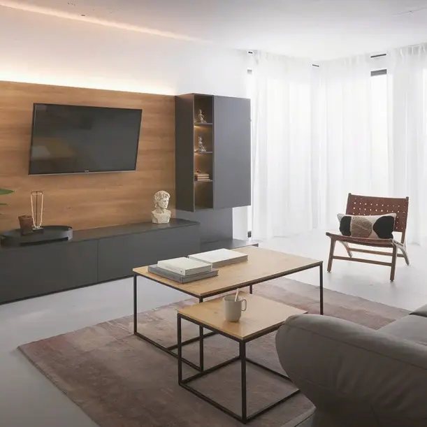 Wohnzimmer mit TV an Holzpaneel, Lowboard und Hängeschrank, Couchtische davor und Sessel neben Fenster
