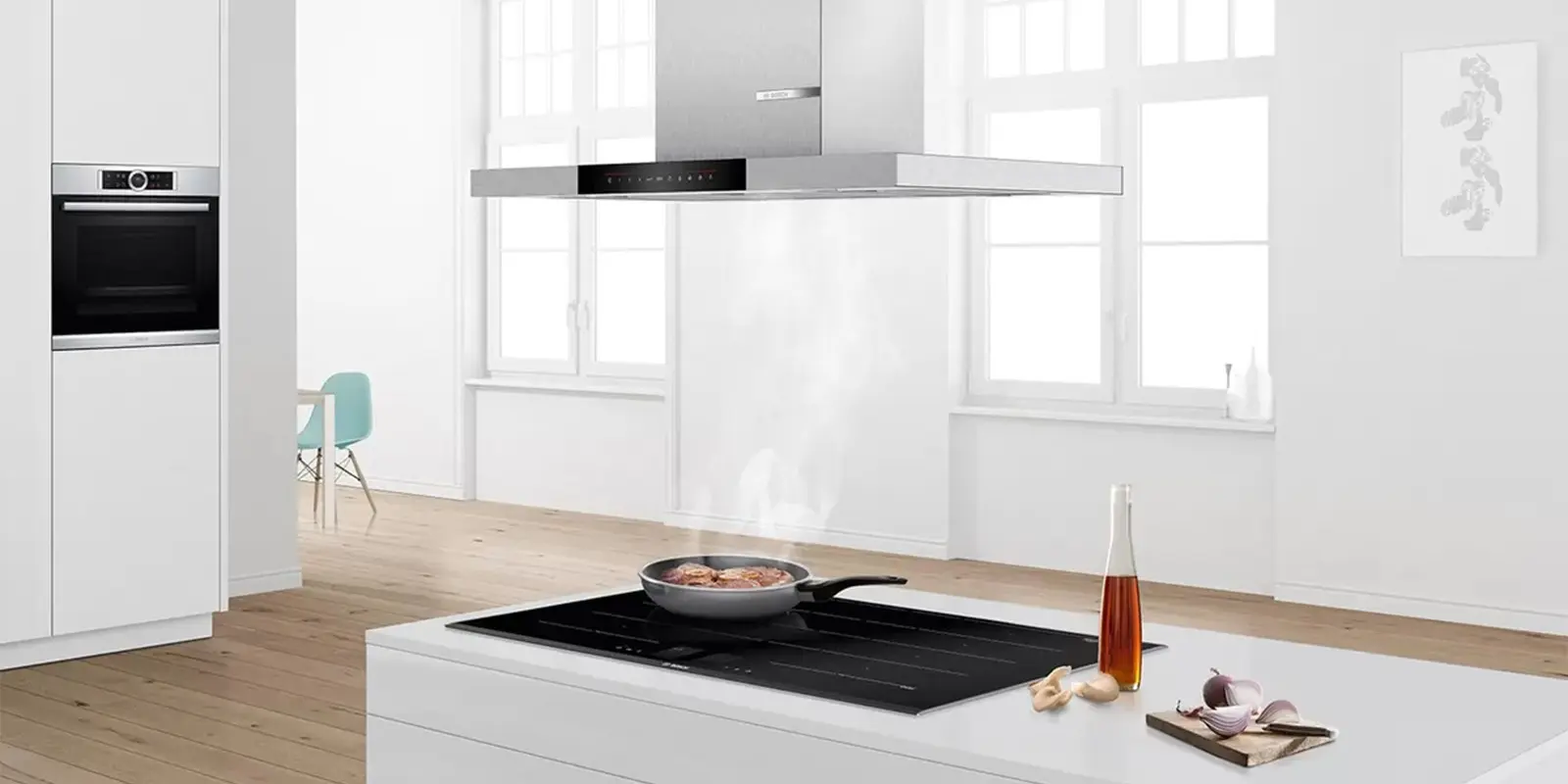 Kochfeld von Bosch auf dem eine Pfanne steht, die das Fleisch brät. Der Dampf wird durch eine an der Decke montierte Abzugshaube abgezogen.&nbsp;