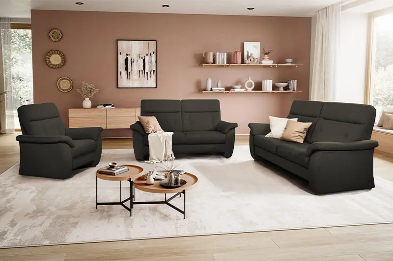 Schwarzer Sessel, neben zwei schwarzer Couch Garnituren in einem hellen gemütlichen Raum.